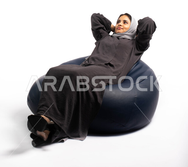 الاستمتاع بوقت الراحة والهدوء , أخذ قسط من الاسترخاء و التأمل, بورتريه لشابة عربية سعودية  خليجية تستلقي على كرسي مريح, إيماءات وتعابير وجه ويدين تدل على الاسترخاء, خلفية بيضاء