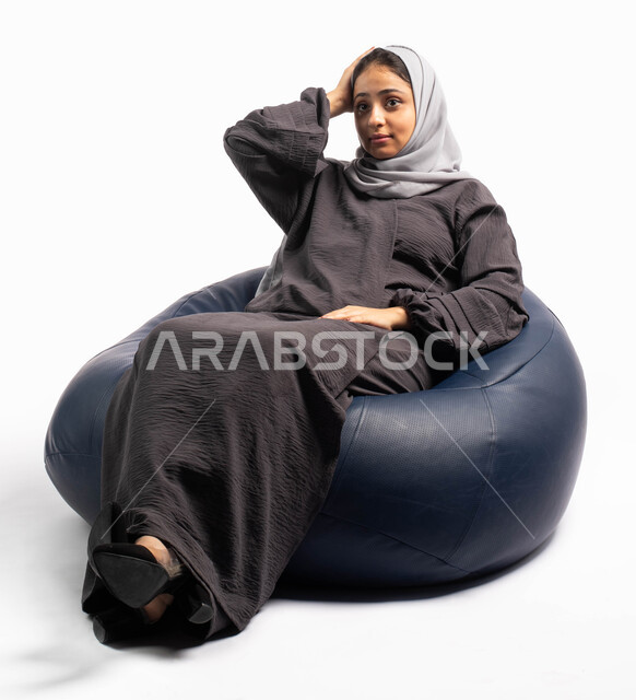 التأمل والتمعن و التفكير بالماضي والمستقبل, إيماءات وتعابير وجه تدل على التفكر و الحيرة , بورتريه لإمرأة عربية سعودية خليجية تجلس على كرسي مريح و تضع يدها على رأسها , خلفية بيضاء