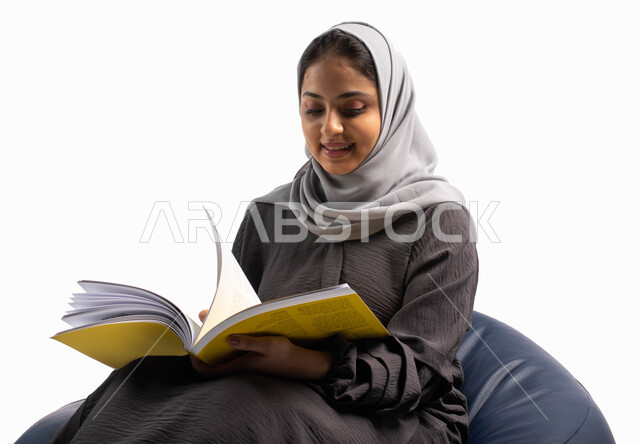 ثقافة التعلم الذاتي, إنجاز الواجبات اليومية, قضاء الوقت بالقراءة والتعلم والتثقف ، بورتريه لإمرأة عربية سعودية خليجية تجلس على كرسي مريح وتحمل بيديها كتاب  ، إيماءات تعبر عن الاستمتاع بقراءة الكتب,  خلفية بيضاء