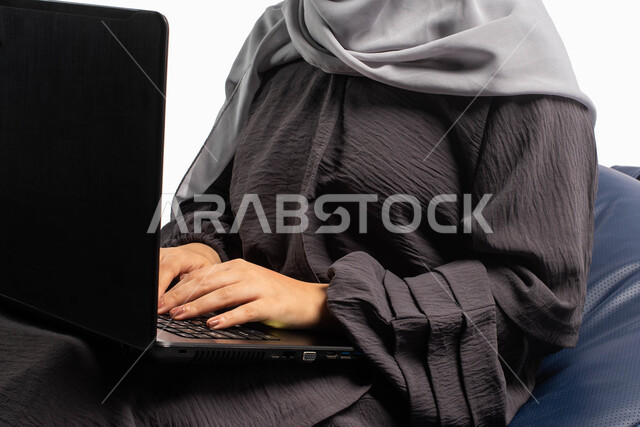 إدارة المشاريع عن بعد, بورتريه صورة مقربة لإمرأة عربية سعودية خليجية تجلس على أريكة مريحة وتستخدم اللابتوب, انجاز مهام العمل عبر الحاسوب, اللعب على اللابتوب, إجراء مكالمات فيديو عبر الإنترنت, قضاء وقت ممتع, خلفيه بيضاء
