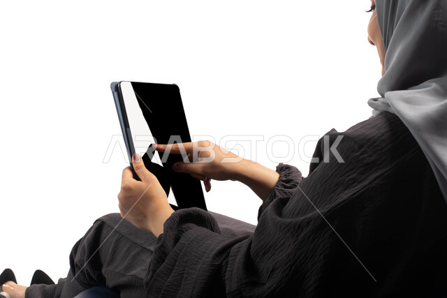 إستخدام اجهزة تقنية حديثة،  بورتريه من الخلف لامرأة عربية سعودية خليجية تتجلس على كرسي مريح تستخدم جهاز التابلت ، التسوق الإلكتروني الآمن، تصفح الإنترنت وإنجاز المهام عن بعد ، الشراء والبيع عبر الاونلاين، خلفية بيضاء 