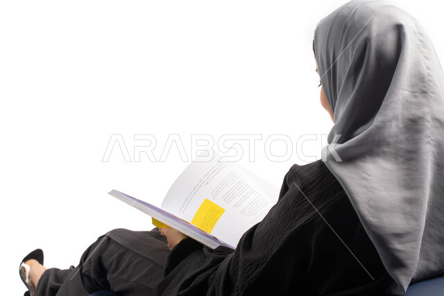 Spending time reading, learning and educating, a portrait from behind of a young Saudi Arabian Gulf woman sitting on a comfortable chair and holding a book in her hands, enjoying reading books, self-learning culture, white background