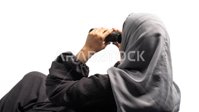 رؤية الاشياء البعيدة عبر المنظار، حب الاستكشاف والمغامرة، بورتريه من الخلف لسيدة عربية خليجية سعودية تجلس على كرسي مريح وتنظر من خلال منظار الرؤية, التخطيط المستقبلي للأهداف و الطموحات، خلفية بيضاء