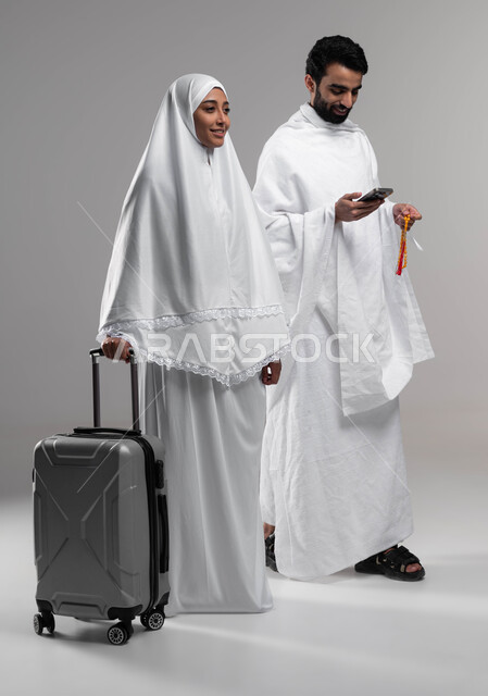 Preparing to travel to perform the rituals of Hajj and Umrah, a close-up portrait of a Saudi Arabian Gulf Muslim couple wearing the Ihram dress, a picture of a Saudi Arab Gulf man carrying a prayer beads and browsing a mobile phone, a woman holding a trav