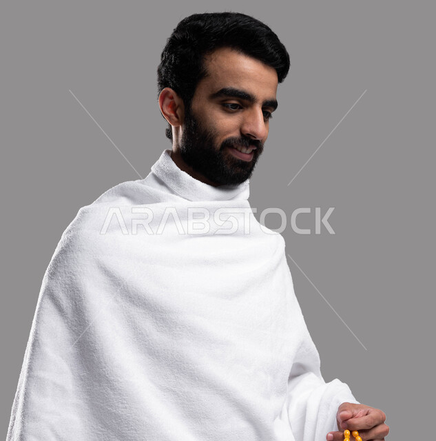 Performing Umrah in Makkah Al-Mukarramah in the holy month of Ramadan, a close-up portrait of a Saudi Arabian Gulf Muslim man wearing Ihram clothes and carrying a yellow rosary, facial gestures indicating happiness, performing Hajj and Umrah rituals, Isla