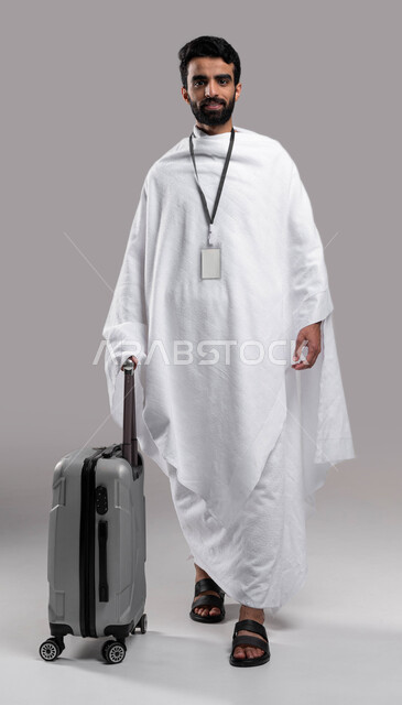  ارتداء بطاقة تعريف بيضاء، الاستعداد للسفر والذهاب لأداء فريضة الحج في مكة المكرمة، شاب مسلم خليجي عربي سعودي يرتدي ملابس الإحرام ويمسك حقيفة السفر، موسم الحج 2023، آداء مناسك الحج والعمرة, إسلاميات وعبادة