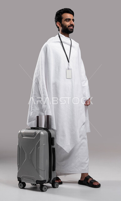  ارتداء بطاقة تعريف بيضاء، الاستعداد للسفر والذهاب لأداء فريضة الحج في مكة المكرمة، شاب مسلم خليجي عربي سعودي يرتدي ملابس الإحرام ويمسك حقيفة السفر، موسم الحج 2023، آداء مناسك الحج والعمرة, إسلاميات وعبادة