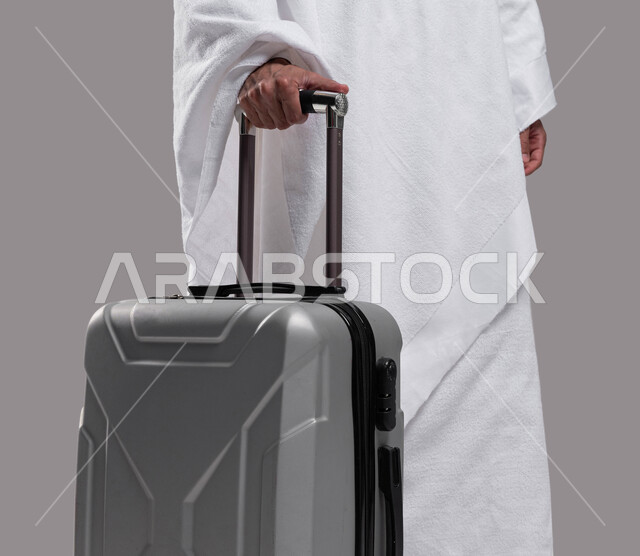 التجهيز و الاستعداد للسفر والذهاب لأداء العمرة في مكة المكرمة في شهر رمضان المبارك ، شاب مسلم خليجي عربي سعودي يرتدي ملابس الإحرام ويمسك حقيفة السفر، آداء مناسك الحج والعمرة, إسلاميات وعبادة