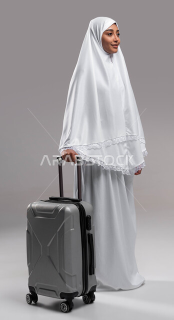 صورة الجسم بالطول الكامل، التجهيز و الاستعداد للسفر والذهاب لأداء العمرة في مكة المكرمة في شهر رمضان المبارك ، بورتريه لامرأة مسلمة خليجية عربية سعودية ترتدي ملابس الإحرام وتمسك حقيبة السفر، آداء مناسك الحج والعمرة, إسلاميات وعبادة