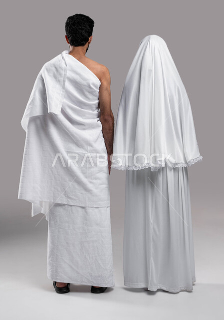 مفهوم الألفة بين الزوجين, زيارة بيت الله الحرام في مكه المكرمه, اداء فريضة الحج والعمره في موسم الحج 2023،  صوره من الخلف لزوجان عربيان خليحيان سعوديان يرتديان ثياب الاحرام، اسلاميات وعباده, صورة الجسم بالطول الكامل, خلفية رمادية