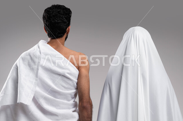 الإكثار من العبادات في الشهر المبارك, مفهوم الألفة بين الزوجين, زيارة بيت الله الحرام في مكه المكرمه, اداء فريضة الحج والعمره في موسم الحج 2023،  بورتريه من الخلف لزوجان عربيان خليحيان سعوديان يرتديان ثياب الاحرام، اسلاميات وعبادة, خلفية رمادية
