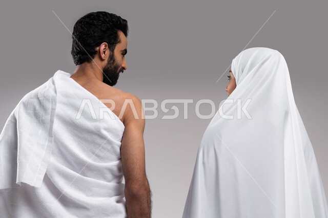 الإكثار من العبادات في الشهر المبارك, مفهوم الألفة بين الزوجين, زيارة بيت الله الحرام في مكه المكرمه, اداء فريضة الحج والعمره في موسم الحج 2023،  بورتريه من الخلف لزوجان عربيان خليحيان سعوديان يرتديان ثياب الاحرام، اسلاميات وعبادة, خلفية رمادية