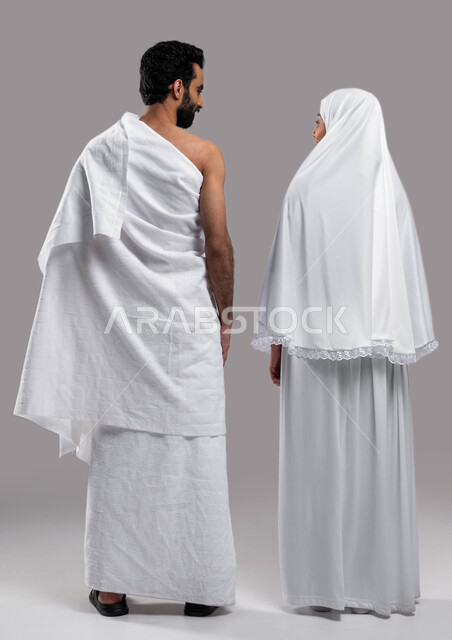 مفهوم الألفة بين الزوجين, زيارة بيت الله الحرام في مكه المكرمه, اداء فريضة الحج والعمره في موسم الحج 2023،  صوره من الخلف لزوجان عربيان خليحيان سعوديان يرتديان ثياب الاحرام، اسلاميات وعباده, صورة الجسم بالطول الكامل, خلفية رمادية