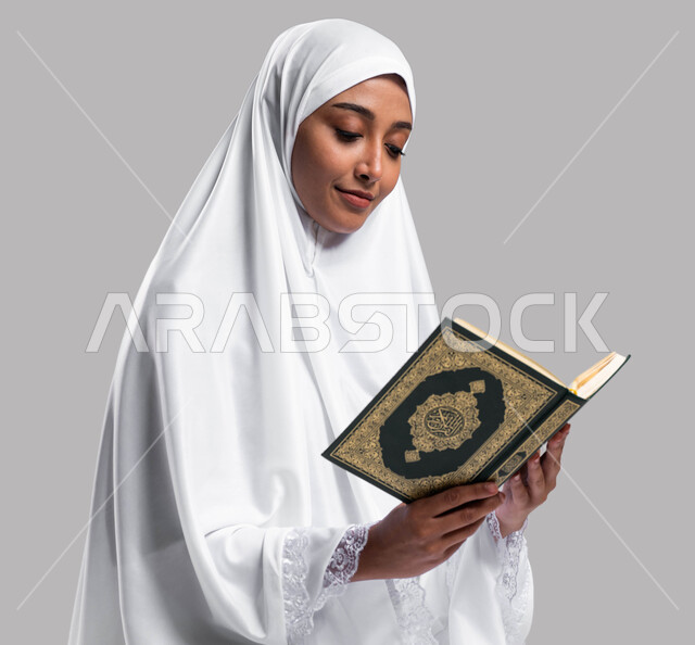 Diligence in worship in the blessed months, performing the rituals of Hajj and Umrah, drawing closer to God by reading the Holy Qur’an and contemplating its meanings, a portrait of a Saudi Arab Gulf woman wearing prayer clothes and holding the Holy Qur’an