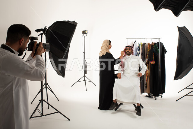 امرأة تقوم بتجميل وتحضير العارض، عبايات نسائية خليجية، تصوير اعلاني تسويقي، مصور محترف عربي سعودي خليجي يقوم بالتقاط صور فوتوغرافية، بورتريه لجلسة تصوير في الاستوديو، كاميرات ومعدات متطورة، خلف الكواليس، خلفية بيضاء