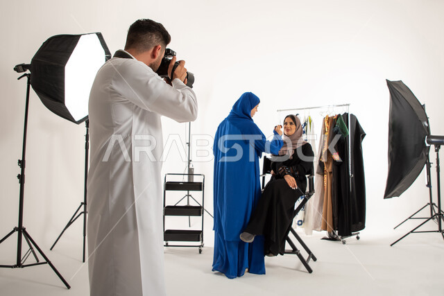 بورتريه لجلسة تصوير في الاستوديو، عبايات نسائية خليجية، مصور عربي سعودي خليجي يقوم بالتقاط صور فوتوغرافية لامرأة تقوم بتجميل عارضة ازياء وموديلات عصرية، تصوير اعلاني تسويقي، كاميرات ومعدات متطورة، خلف الكواليس، خلفية بيضاء