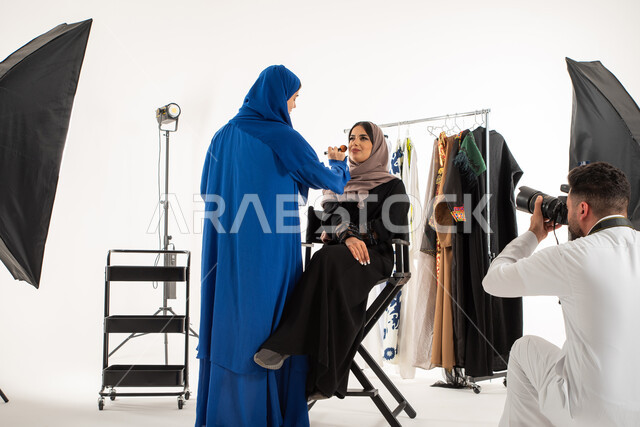 عبايات نسائية خليجية، امرأة تقوم بتجميل عارضة ازياء وموديلات عصرية، بورتريه لجلسة تصوير في الاستوديو، مصور عربي سعودي خليجي يقوم بالتقاط صور فوتوغرافية، تصوير اعلاني تسويقي، كاميرات ومعدات متطورة، خلف الكواليس، خلفية بيضاء