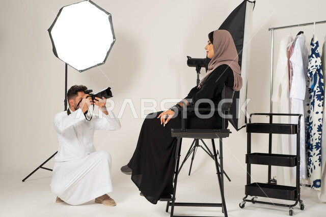 تصوير اعلاني تسويقي، عارضة ازياء وموديلات عصرية، بورتريه لجلسة تصوير في الاستوديو، مصور عربي سعودي خليجي يقوم بالتقاط صور فوتوغرافية لامرأة تجلس على الكرسي، عبايات نسائية خليجية، خلف الكواليس، كاميرات ومعدات متطورة، خلفية بيضاء
