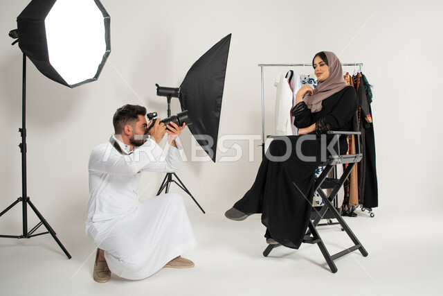 عبايات نسائية خليجية، عارضة ازياء وموديلات عصرية، بورتريه لجلسة تصوير في الاستوديو، مصور عربي سعودي خليجي يقوم بالتقاط صور فوتوغرافية لامرأة تجلس على الكرسي، كاميرات ومعدات متطورة، خلف الكواليس، تصوير اعلاني تسويقي، خلفية بيضاء