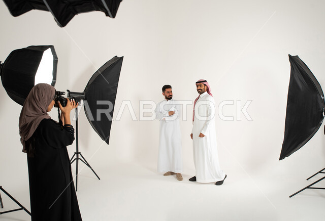 Behind the scenes, marketing advertising photography, two men dressed in traditional Saudi clothing, a professional Saudi Arabian Gulf photographer taking photographs, a portrait of a photo session in the studio, advanced cameras and equipment, white back