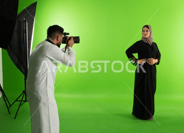 تصوير اعلاني تسويقي، عارضة أزياء وموديلات عصرية، مصور محترف عربي سعودي خليجي يقوم بالتقاط صور فوتوغرافية لامرأة ترتدي عباءة نسائية خليجية، كاميرات ومعدات متطورة، كروما لجلسة تصوير في الاستوديو، خلفية شاشة خضراء، خلف الكواليس
