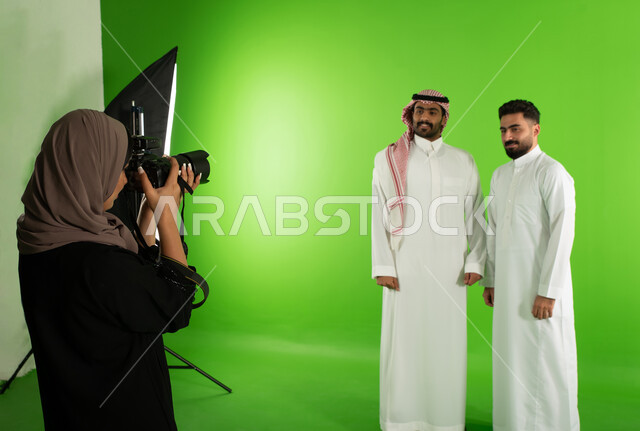 Two Saudi Arab Gulf men dressed in traditional Saudi clothing, marketing advertising photography, a professional Saudi photographer taking photographs, advanced cameras and equipment, chroma for a photo session in the studio, green screen background, behi
