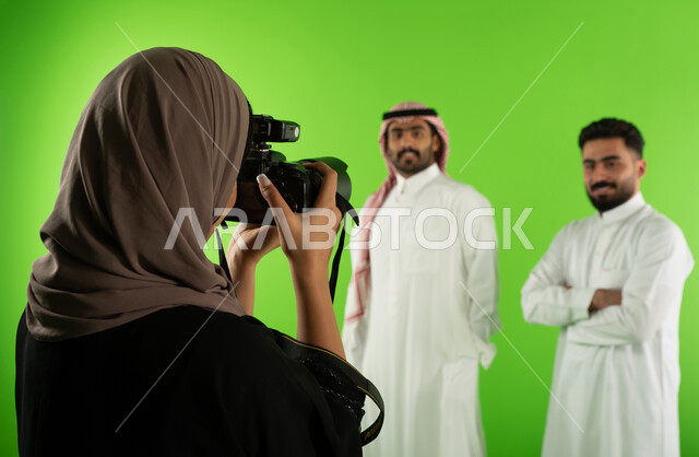 كاميرات ومعدات متطورة، تصوير اعلاني تسويقي، مصورة محترفة عربية سعودية خليجية تقوم بالتقاط صور فوتوغرافية لرجلان يرتديان الزي السعودي التقليدي، كروما لجلسة تصوير في الاستوديو، خلفية شاشة خضراء، خلف الكواليس