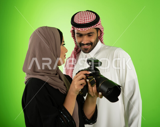مصورة عربية سعودية خليجية تقوم بانتقاء الصور الفوتوغرافية مع العارض، مراجعة واختيار أفضل الصور من الكاميرا، كروما جلسة تصوير في الاستوديو، خلفية شاشة خضراء، كاميرات إلكترونية متطورة، خلف الكواليس