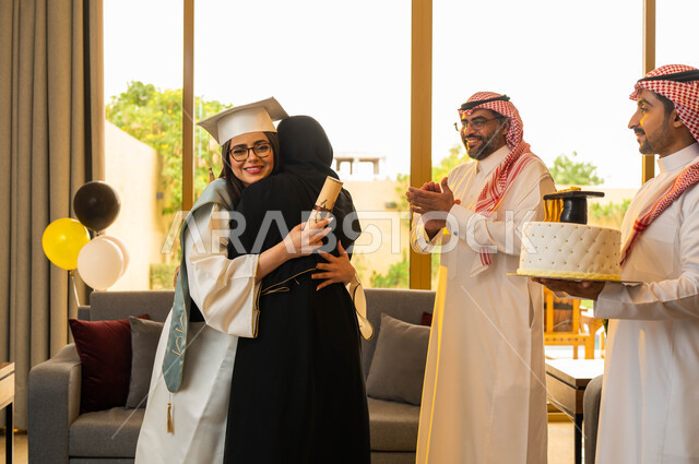 قالب الجاتوه المزين بقبعة التخرج، ام تقوم بمعانقة ابنتها فرحا بتخرجها، عائلة سعودية خليجية عربية تحتفل بتخرج ابنتها من الجامعة، خريجة جامعية ترتدي النظارات الطبية وملابس التخرج وتمسك شهادة التخرج، ايماءات وجه تدل على السعادة، التعليم في السعودية