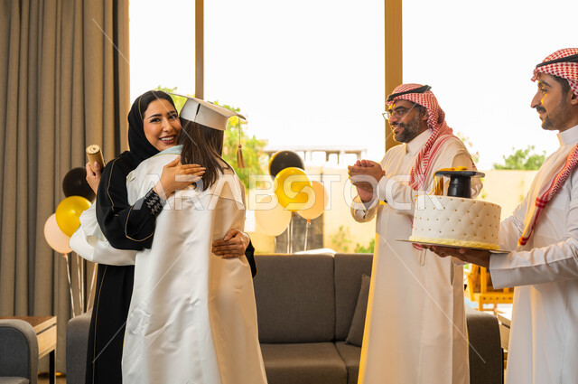 A mother embraces her daughter with joy at her graduation from the university with distinction and distinction, a Saudi Gulf Arab family celebrates her daughter's graduation from the university, a cake mold decorated with a graduation hat, a university gr
