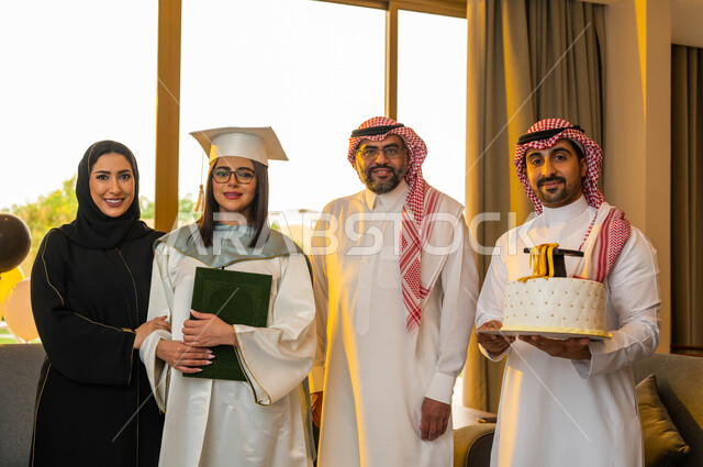 خريجة جامعية ترتدي النظارات الطبية وملابس التخرج، قالب الجاتوه المزين بقبعة التخرج، شهادة النجاح والتفوق، ايماءات وجه تدل على السعادة، عائلة سعودية خليجية عربية تحتفل بتخرج ابنتها من الجامعة في احدى الشاليهات، التعليم في السعودية