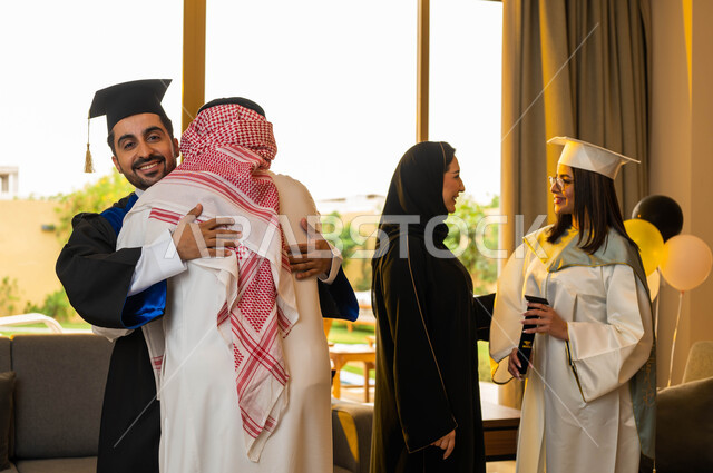 رجل عربي سعودي خليجي يعانق ابنه فرحا بتخرجه من الجامعة بتفوق وامتياز، عائلة سعودية خليجية عربية سعيدة تحتفل بتخرج ابنائها من الجامعة، خريج جامعي يرتدي ملابس التخرج ويمسك شهادة التفوق والنجاح، ايماءات وجه تدل على السعادة، التعليم في السعودية