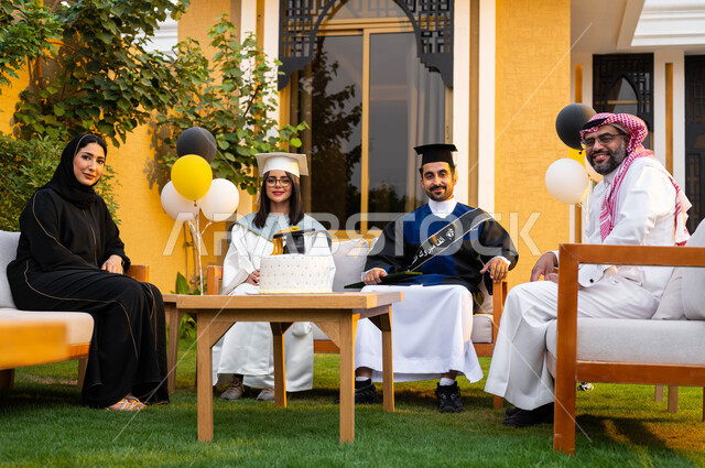 قالب الجاتوه المزين بقبعة التخرج، عائلة سعودية عربية خليجية تحتفل بتخرج الابناء في احدى الشاليهات، خريج وخريجة جامعيين يرتديان ملابس التخرج، ايماءات وجه تدل على السعادة والفرح، التعليم في السعودية