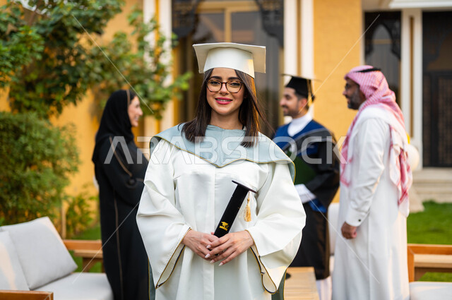 خريجة جامعية عربية خليجية سعودية ترتدي ملابس التخرج وتمسك شهادة النجاح والتفوق، شابة بايماءات وجه تدل على السعادة والفرح، عائلة سعودية خليجية عربية سعيدة تحتفل بتخرج ابنائها من الجامعة، التعليم في السعودية