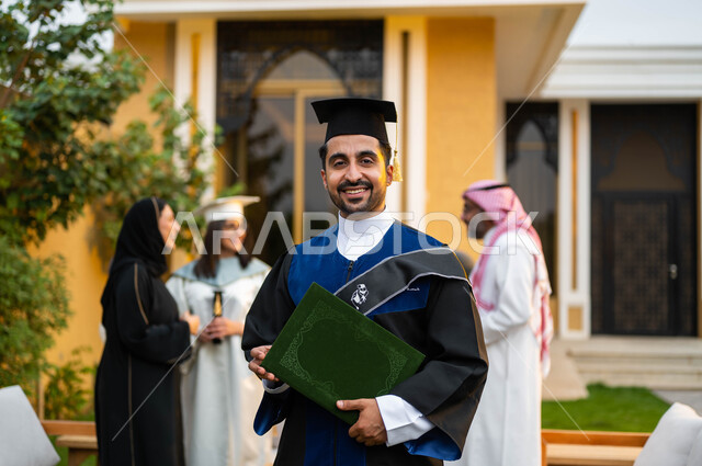 خريج جامعي بايماءات وجه تدل على السعادة والفرح، شاب عربي خليجي سعودي يرتدي ملابس التخرج ويمسك شهادة النجاح والتفوق، عائلة سعودية خليجية عربية سعيدة تحتفل بالتخرج، التعليم في السعودية