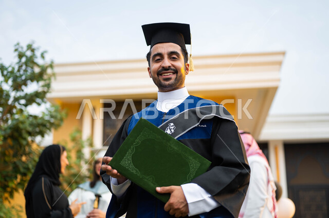 شاب عربي خليجي سعودي يرتدي ملابس التخرج ويمسك شهادة النجاح والتفوق ...
