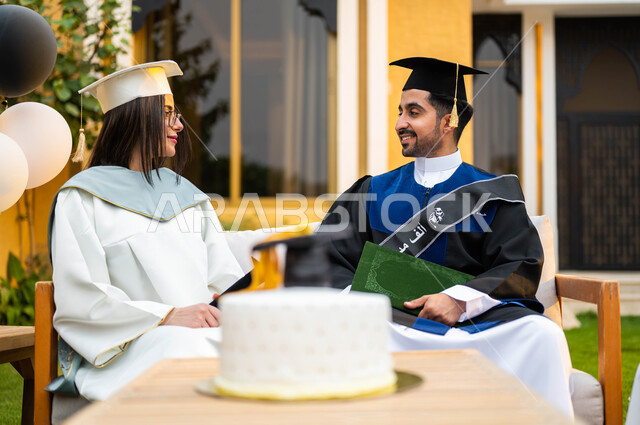 كيكة الاحتفال بالتخرج، خريج وخريجة جامعيين سعوديان خليجيان عربيان يرتديان ملابس التخرج ويمسكان شهادة النجاح والتفوق، الاحتفال بالتخرج في احدى الشاليهات السياحية في السعودية، ايماءات وجه تدل على السعادة، التعليم في السعودية