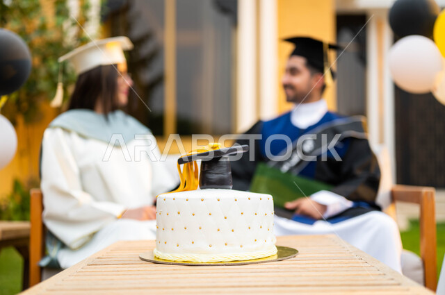 الاحتفال بالتخرج في احدى الشاليهات السياحية في السعودية، كيكة الاحتفال بالتخرج، خريج وخريجة جامعيين سعوديان خليجيان عربيان يرتديان ملابس التخرج ويمسكان شهادة النجاح والتفوق،ايماءات وجه تدل على السعادة، التعليم في السعودية