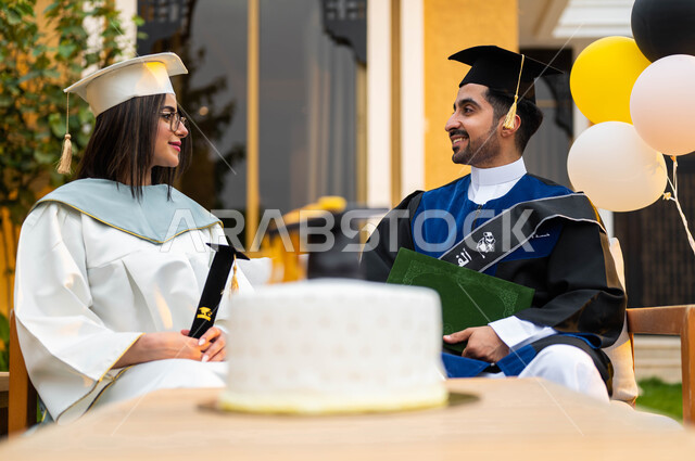 الاحتفال بالتخرج في احدى الشاليهات السياحية في السعودية، خريج وخريجة جامعيين سعوديان خليجيان عربيان يرتديان ملابس التخرج ويمسكان شهادة النجاح والتفوق، كيكة الاحتفال بالتخرج، ايماءات وجه تدل على السعادة، التعليم في السعودية