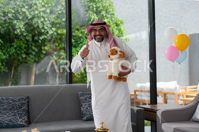 ايماءات تدل على علامة الجودة و السعادة, رجل كبير السن عربي خليجي سعودي يرتدي الزي السعودي التقليدي و يحمل بيده دمية على شكل خاروف عيد الاضحى المبارك, أعياد ومناسبات اسلامية, الاحتفال بالعيد السعيد .