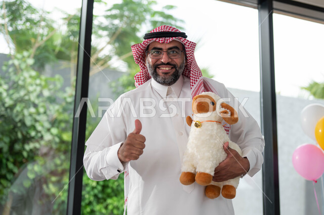 ايماءات تدل على علامة الجودة و السعادة, رجل كبير السن عربي خليجي سعودي يرتدي الزي السعودي التقليدي و يحمل بيده دمية على شكل خاروف عيد الاضحى المبارك, أعياد ومناسبات اسلامية, الاحتفال بالعيد السعيد .