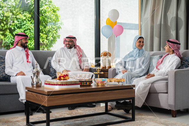 تبادل الحوارات و النقاشات بين أفراد العائلة, ايماءات تدل على الفرح والسعادة, تجمع عائلي لعائلة عربيه خليجية سعودية تحتفل بعيد الاضحى المبارك في غرفة المعيشة ,قضاء اوقات ممتعة مع الابناء, أعياد ومناسبات اسلامية .