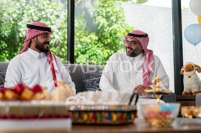 الاحتفال  في عيد الاضحى المبارك مع الابناء ,رجل مسن عربي خليجي سعودي مع ابنه يرتديان الثوب والشماغ السعودي,  أجواء العيد في المجتمع العربي السعودي, ايماءات تدل على السعادة, تبادل الاحاديث والنقاشات, اعياد ومناسبات اسلامية