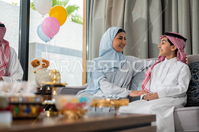 تبادل الاحاديث و الحوارات مع الابناء, ولد عربي خليجي سعودي مع والدته في غرفة المعيشة يحتفلون في عيد الاضحى المبارك, يماءات تدل على الفرح والسعاده, الزيارات و التجمعات الاسريه, الأعياد والمناسبات الاسلامية السعيدة .