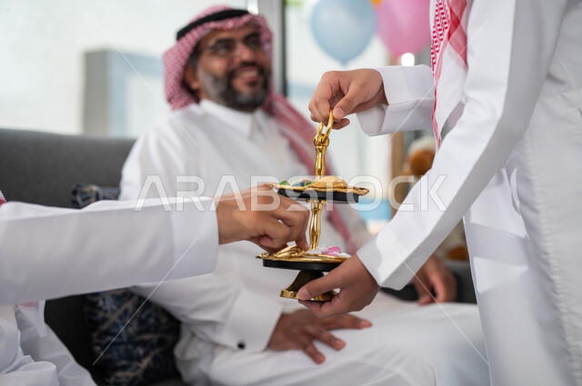 صورة مقربة لتقديم حلوى وكعك العيد , حسن استقبال واكرام الضيوف, عائلة عربية سعودية خليجية تحتفل بالعيد, ايماءات تدل على الفرح والسعاده, الزيارات و التجمعات الاسريه, التهنئه بقدوم العيد ,الأعياد والمناسبات الاسلامية السعيدة .