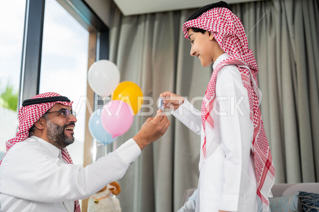 تقديم العيدية للأحفاد, أعياد ومناسبات اسلامية, أجواء العيد في المجتمع العربي السعودي,  التجمعات والزيارات الاسرية في عيد الاضحى المبارك, ايماءات تدل على السعاده , رجل مسن عربي خليجي سعودي يحتفل في العيد مع الابناء في ايام العيد السعيد في السعوديه