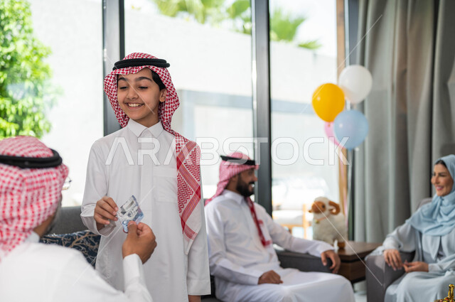 أجواء العيد في المجتمع العربي السعودي, تقديم العيدية للأحفاد, التجمعات والزيارات الاسرية في عيد الاضحى المبارك, ايماءات تدل على السعاده , رجل مسن عربي خليجي سعودي يحتفل في العيد مع الابناء في ايام العيد السعيد في السعوديه, أعياد ومناسبات اسلامية