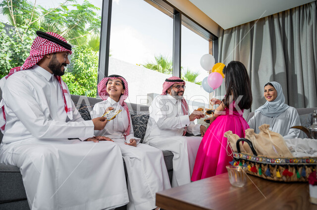حسن استقبال و اكرام الضيوف, فتاة عربية خليجية سعودية تقوم بتقديم حلويات عيد الاضحى المبارك, أعياد ومناسبات اسلامية , ايماءات تدل على السعادة, تجمع اسري لعائلة تجلس في غرفة المعيشة وتحتفل في العيد السعيد