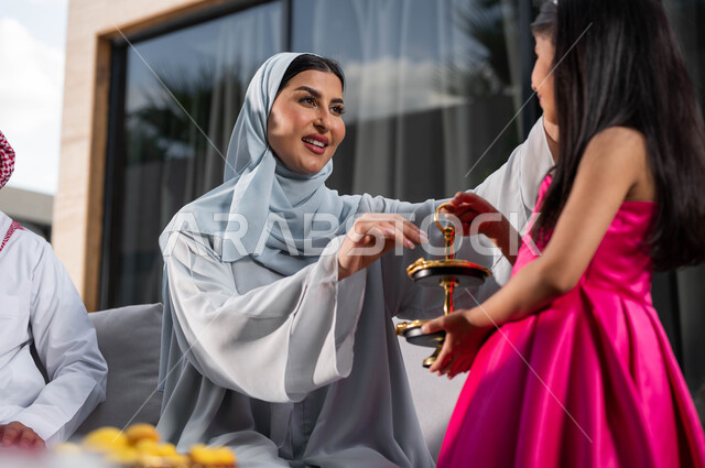 Offering chocolate pieces, a veiled Saudi Arabian Gulf woman, welcoming and honoring the guests, spending good times in one of the luxurious chalets, family meeting and celebrating with the children in the happy Eid, Islamic holidays and events