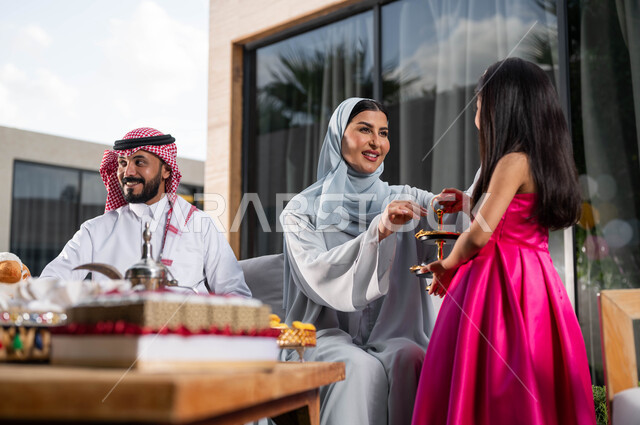 Offering chocolate pieces, a veiled Saudi Arabian Gulf woman, welcoming and honoring the guests, spending good times in one of the luxurious chalets, family meeting and celebrating with the children in the happy Eid, Islamic holidays and events